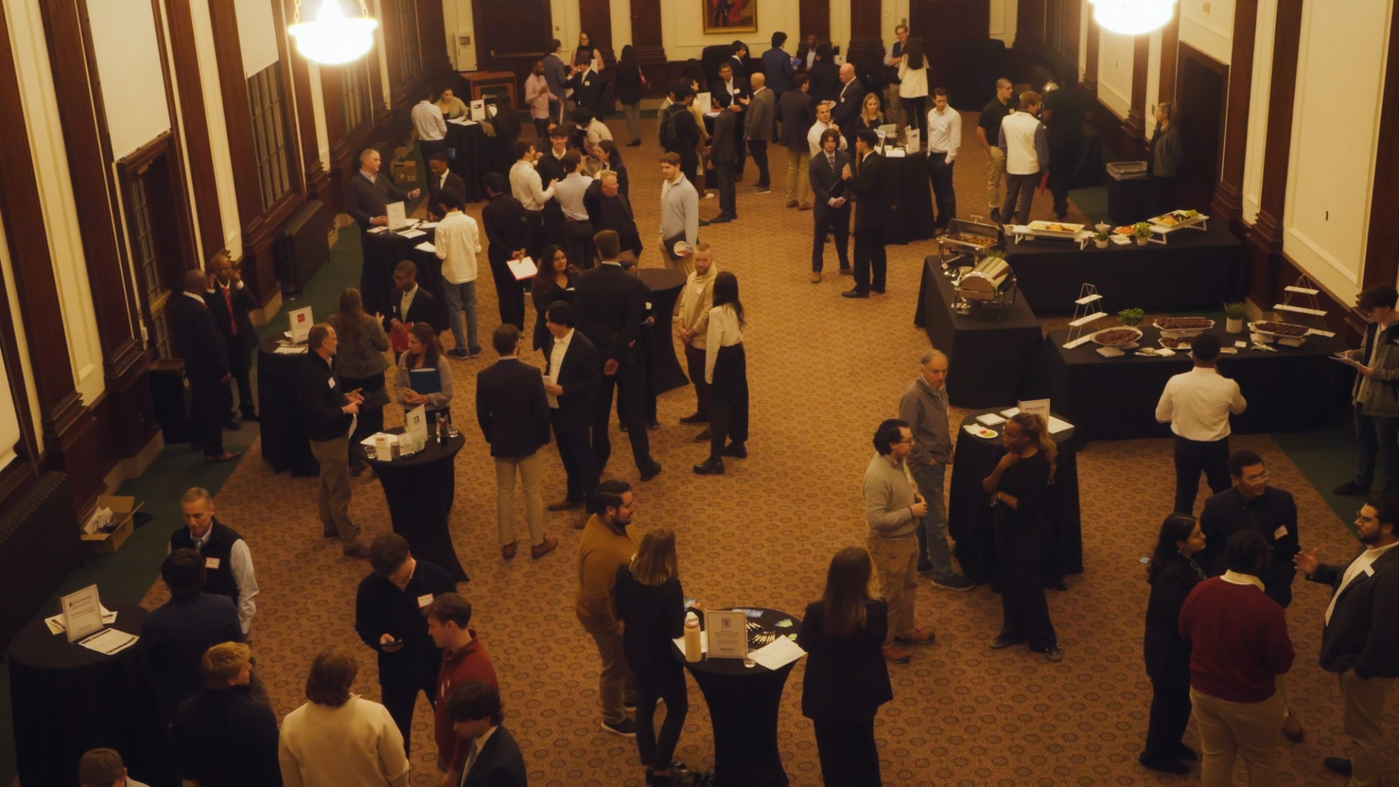 Small crowd of well dressed people standing in a room with tables of food