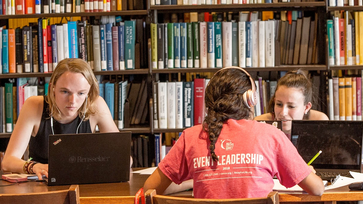 Three students work at laptops in the library