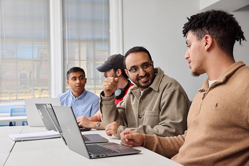 Students work at laptops with a professor