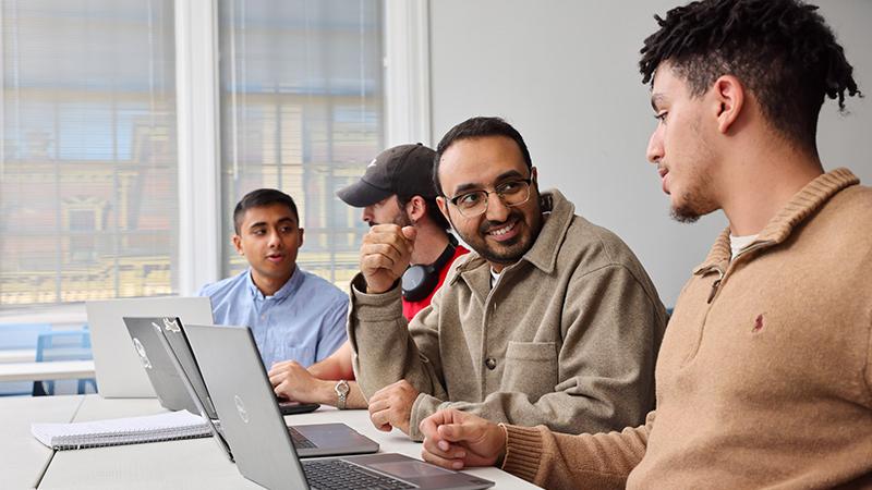 Students work at laptops with a professor