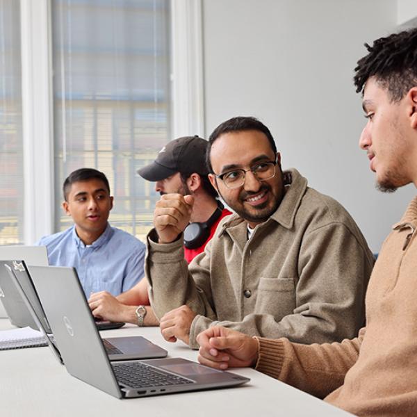 Students with laptops open work with a professor